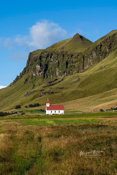 Reyniskirkja Beneath the Cliffs of Vík Iceland

This peaceful scene captures Reyniskirkja, the beloved white church with its classic red roof, resting quietly at the base of the lush green mountains near Vík í Mýrdal, Iceland. The surrounding hills rise dramatically behind the church, their rugged cliffs and velvet grasslands forming a spectacular natural backdrop. Soft afternoon light sweeps across the fields, highlighting the textures of the landscape and guiding the eye toward the simple beauty of the rural church.

Reyniskirkja, built in 1929, remains one of the most charming and recognizable churches in South Iceland. Set against the towering mountains and open farmland, it represents the quiet resilience and deep cultural heritage of this remote coastal region. The contrast between the stark white church and the vivid green cliffs makes this one of the most photogenic and iconic scenes near Vík.

Image:
https://fineartamerica.com/featured/reyniskirkja-beneath-the-cliffs-of-vik-iceland-wayne-moran.html

Read more:
https://waynemoranphotography.com/blog/chasing-light-across-iceland-our-21-day-adventure/

#Reyniskirkja #church #architecture #Vik #Iceland #nature #travelPHotogrpahy #Landscape #art #fineart 

#ayearforart #buyintoart
