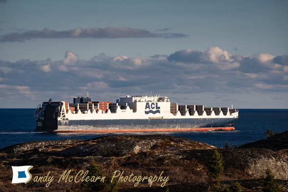 Large container ship underway at sea with a rocky landscape in the foreground. 