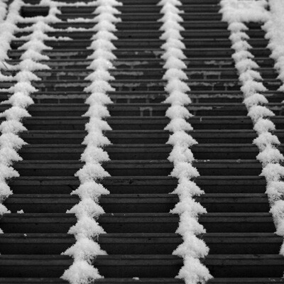 細かく雪が積もったグレーチングのクローズアップ写真。積雪が格子の端に沿って白い山型や三角形の模様を作り出し、繰り返しのパターンを強調している