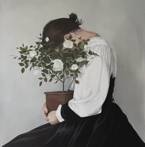 A person with dark hair is seated, leaning forward with their head down, partially obscured by a potted plant bearing white flowers. They are dressed in a white blouse with a black skirt. The background is a light gray.