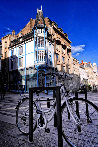 Blue 1800s building with turret-style corner on an urban street with a white bicycle in the foreground