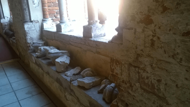 Photo. Broken and damaged rock decorative pieces, placed on the sitting ledge in front of a glass-less window in a neat order. Sun is glaring through the window, making it hard to look at.