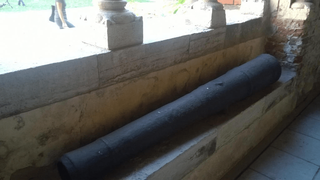 Photo of an old cannon, placed on a sitting ledge by the glass-less window, where the sun is shining through, reflecting on the stones.