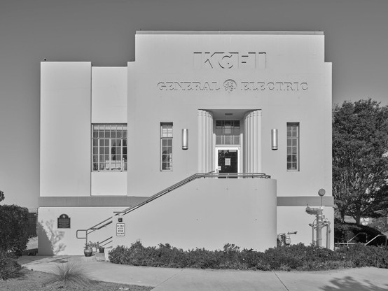 A small concrete building with a staircase leading to a door set back by decorative columns. Above the door, "KGEI / General Electric" is inlayed into the concrete.