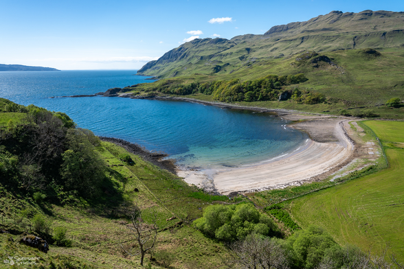 photo down onto a white sandy beach embedded between green hills