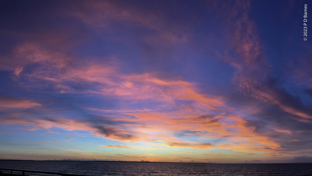 Sunset. Drifts of wispy clouds over the sea, all lit bright pink by the just-set sun against a startling blue sky.