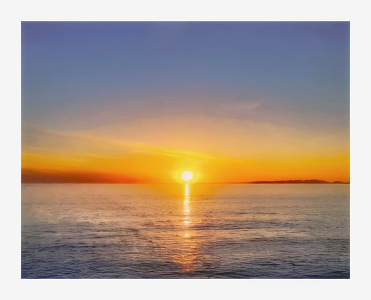A scenic view of a sunset over the atlantic ocean (Galway Bay). The sun is positioned near the horizon with golden light that reflects off the water's surface. The sky transitions from a blue at the top to a warm orange near the horizon. A distant landmass (County Galway) is visible on the right hand side of the photo.