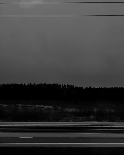 Dark landscape with a silhouette of trees and a lone radio tower against a cloudy sky. Lines of a highway stretch in the foreground.
