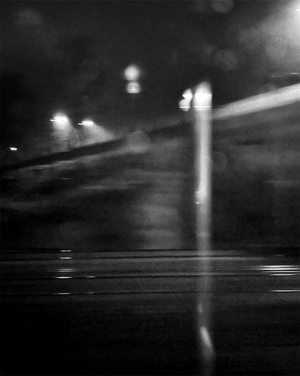 A monochromatic image capturing blurred street lights and reflecting rails in dark, creating a moody and atmospheric scene.