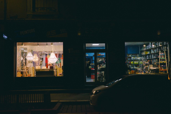Magasin "espace revêtements" à double vitrine : à gauche lustres à pendeloques et guirlandes lumineuses, à droite pots de peintures.