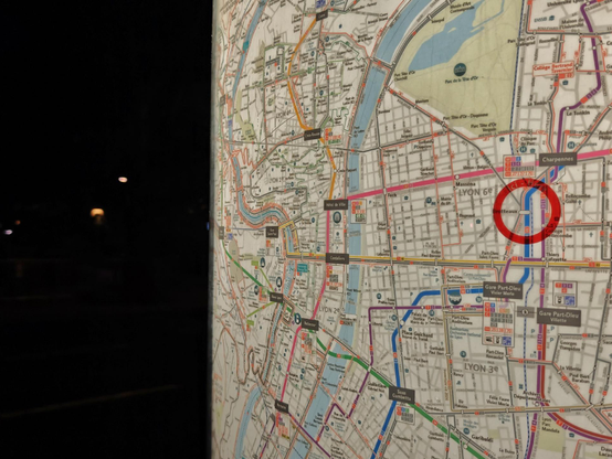 A nighttime phote of an illuminated city map with a red circle marking a location.