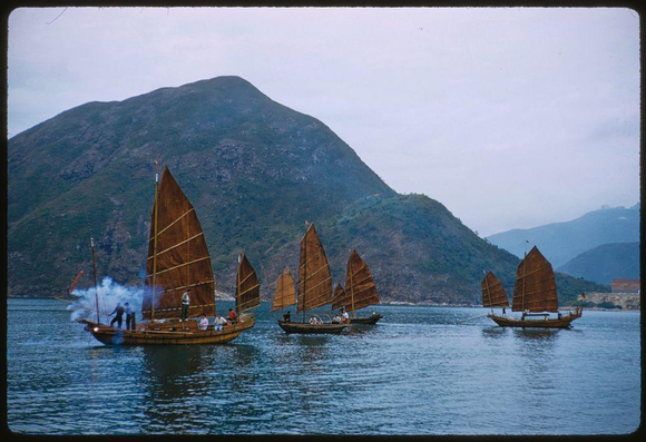 image shows five wooden sailing boats with large brown sails on water in front of a green mountain range. The photograph is from Hong Kong, taken by Toni Frissell for Sports Illustrated magazine and dated July 1959. It depicts sightseeing activities featuring traditional Chinese vessels navigating through the waters near hilly terrain.