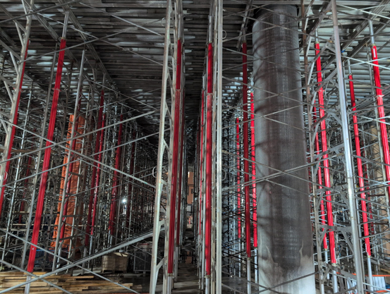 Pronounced vertical silver and red poles with silver diagonal criss-crossing  poles filling the space of the nascent first floor of the tower. A structural pillar to the right throws off the symmetry