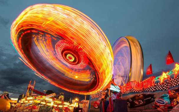 Fairground at dusk with dizzying speeding lights.
Photograph by Jason Chen