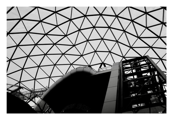 A black and white photo looking up at a glass dome over a shopping centre.