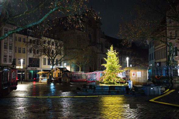 Fußgängerzone in Bamberg. ein Weihnachtsbaum mittig. Rechts der Gabelmann im dunkeln. Strom Leitungen unter Schutz am Boden. Kaufäuser und eine Kirche außsenrum. Weihnachtsstände. Beleuchtungen und Lichter. Ein paar Bäume.
