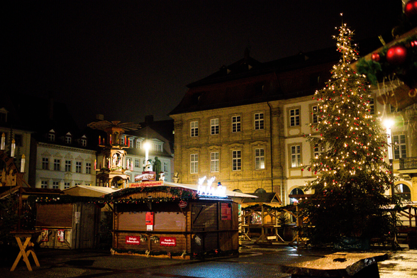 rechts ein Weihnachtsbaum. Marktplatz. Weihnachtsmarktstände. Alte Kaufhäuser um Hintergrund. Dunkel Lichter und Beleuchtung.
