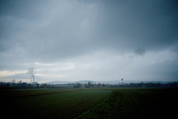 Wiese Feld. in der Ferne ist der Autohof Breitengüßbach. ein paar Bäume Fern. Es raucht links. ein Mast mit Werbung zu erahnen. Wolken mit Strucktur