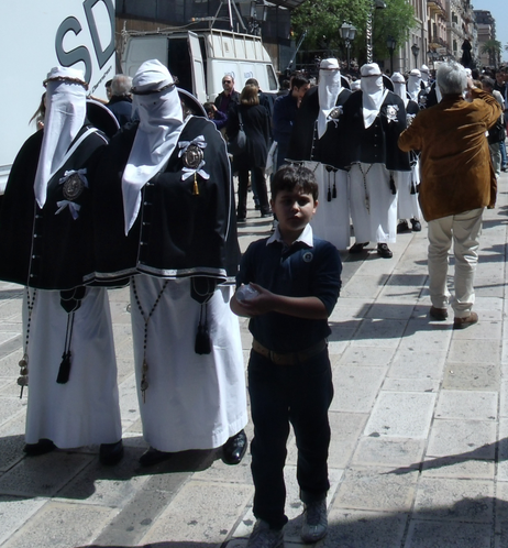 A boy stares at the camera, in front of a procession of robed walkers.