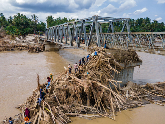 Residents clamber over debris to cross on a newly built bridge connecting Aceh and North Sumatra after flash floods.