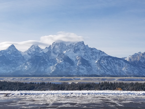 A snow covered set of mountains with a parking lot and a line of trees