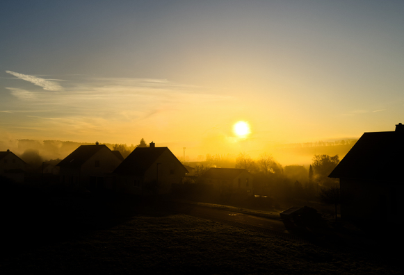 Ein Dorf wird bei Sonnenaufgang in goldenes Licht und feinen Nebel getaucht.