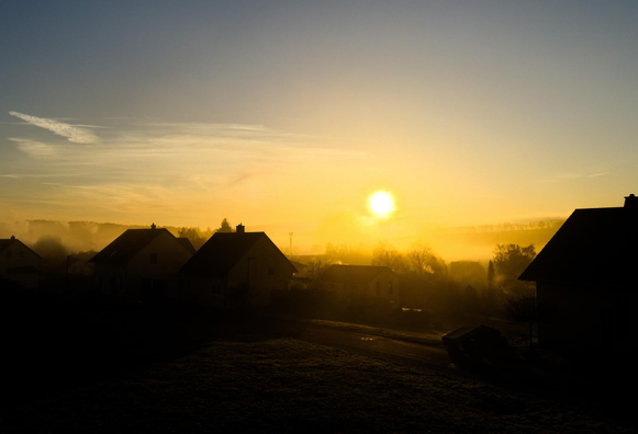 A village is bathed in golden light and fine mist at sunrise.