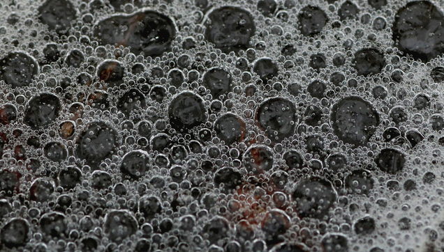 Macro photograph of transparent, bluish water bubbles, almost frozen, on the surface of a stream, resembling more soap foam. Red conifer needles are visible underwater through the bubbles.

Photographie macro de bulles d'eau transparentes et bleutées presque gelées à la surface d'un ruisseau, ressemblant davantage à de la mousse de savon. Des aiguilles de conifères rouges sont visibles sous l'eau à travers les bulles.