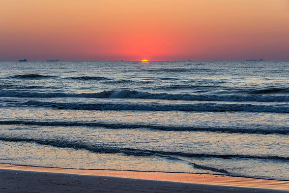 The sun begins to rise with it just breaking on the horizon over the Gulf of Mexico, casting a warm glow on the water. Ships dot the horizon, adding depth to the tranquil scene. ©Debra Martz, All Rights Reserved
