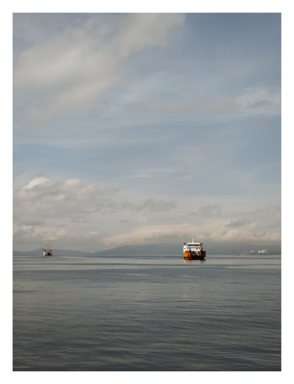 Two ferries navigating calm, gray-blue water beneath an expansive, cloudy sky. A large orange and white ferry is prominent on the right, balanced by a distant mountainous coastline. - Google Gemini Latest