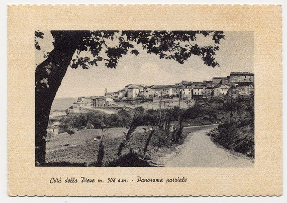 The image shows a vintage black and white photograph depicting an old European village nestled on a hillside. A prominent tree branch with sprawling leaves frames the upper left corner of the picture, leading down to a cobblestone path winding through the scene towards buildings clustered atop the slope in various shades of gray that convey their age and texture. The architectural style suggests historical significance typical of regions like Tuscany or Umbria in Italy.

At the bottom center of the photograph is handwritten text providing location details: "Città della Pieve m. 508 d.m." which translates to "City of Pieve, at an elevation of approximately 508 meters above sea level" and "- Panorama parziale," meaning "- Partial panorama."

In a smaller font below the image is additional handwritten text that reads: "Città della Pieve m. 508 d.m." which appears to be reiterating or emphasizing the elevation detail mentioned at the bottom center.

The overall aesthetic of the photograph suggests it could have been used as postcard material, capturing a quaint and picturesque view typical for tourism promotion during its time.