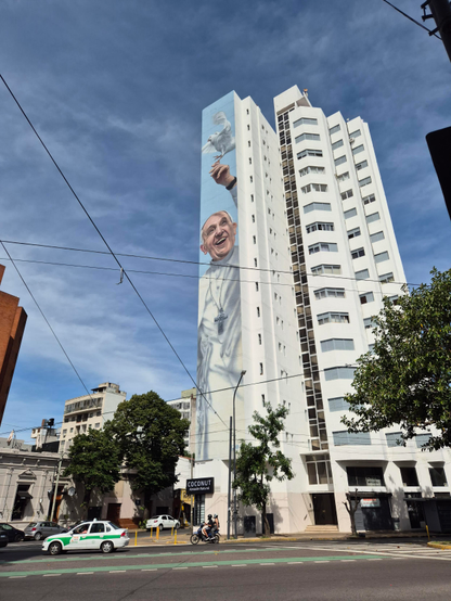 A very high residential building qith a giant mural of Pope Benedict along one narrow wall. 