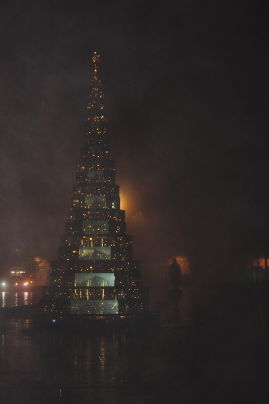 Photo du sapin en verre, illuminé, de la place de l'hôtel de ville à Bordeaux.
Elle est prise avant le lever du jour, avec du brouillard.
Le flash renforce la brume devant l'appareil et le reste est assombri. Les lumières, du sapin, des lampadaires et des immeubles alentours, ressortent orange.

Dans le fond, on aperçoit la silhouette d'une statue, elle est visible grâce à la luminosité du bâtiment derrière elle.