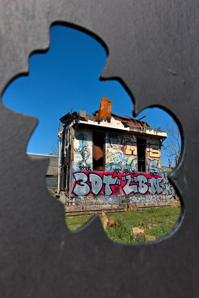 Photo d'un ancien poste d'aiguillage à Bercy en partie détruit vu à travers un trou en forme de nuage découpé dans une palissade