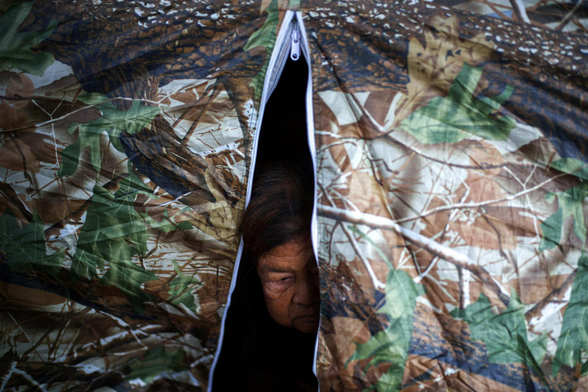 A woman looks out from her tent at a temporary shelter.