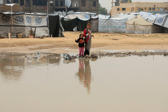 Displaced Palestinian children stand next to a puddle in a tent camp on a rainy day in Khan Younis, southern Gaza Strip. 