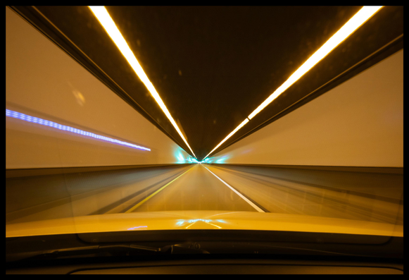 A 1 second exposure of the Tom Lantos Tunnel, under Montara Mountain, on Highway 1 just south of San Francisco. Shot through a car windshield using an ultrawide lens. 

Vaguely resembling a jump to warp speed, beams of light shoot out past the camera from a distant point in the center of the frame. The majority of the light is gold... lighting the walls of the tunnel, the roadway, and the hood of the car. There is a streak of purple on the left wall of the tunnel... and smears of teal color closer to the vanishing point in the center.

It's all very satisfying to look at, said the guy in the chair (me) who likes to shout Engage whenever he starts driving his car.