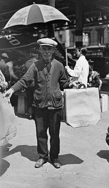 A vendor of paper shopping bags holding up his wares, New York City, 1920s. An advertising slogan on an umbrella in the background reads 'All Eyes Are on Bloomingdales'. (Photo by P. L. Sperr/Frederic Lewis/Archive Photos/Getty Images).