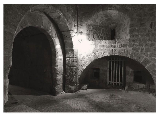 Black and white photo of a small barred wooden gate over a cell within medieval castle walls.