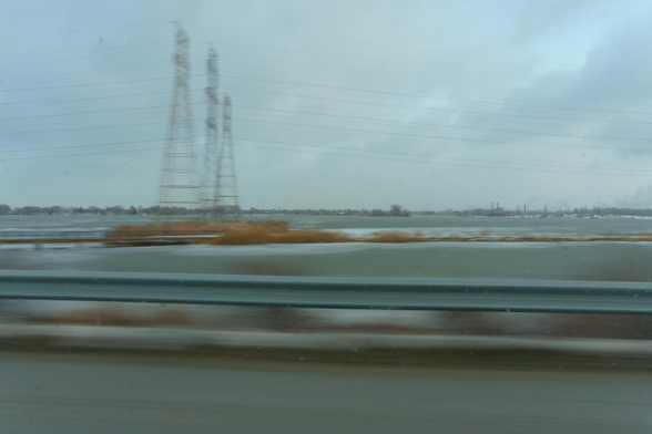 Skyway as it bisects Wolf Lake. In the distance, we see BP's Whiting Refinery turning Canadian tar sands into refined petroleum and plumes of exhaust. Power lines traverse the sky above the bike path. 