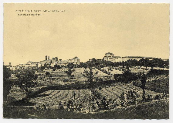 The image depicts a monochromatic panorama of Città della Pieve, an old town with historic architecture. The photo appears to be from the early 20th century based on its style and paper quality. It shows various buildings, including what seems like churches or public structures distinguished by their towers and domes.

In the foreground, there is a rural landscape characterized by agricultural fields that appear fallow without any crops growing at the time of this photograph was taken. There are also clusters of trees scattered across these open lands and on rolling hills leading up to the town's buildings in the background. The terrain seems hilly with patches of vegetation.

The image captures both urban and rural elements, showcasing a harmonious blend between human settlement and natural landscapes typical of smaller Italian towns during that era. There is visible text at the top indicating "Città della Pieve" along with an altitude measurement (508 meters) and a description stating it's a northern panoramic view.

The paper on which this photograph rests shows signs of aging, including slight discoloration and creasing, adding to its historical value.