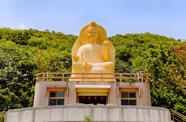 Top of a temple with a large golden bodhisattva statue against green hills.