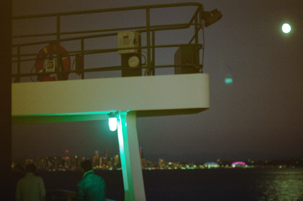 A dark night on the Seattle ferry with the moon and lights illuminating a man in a jacket