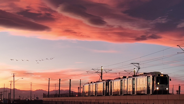 A commuter train stands silently before a hell of a sunset in front of the Rocky Mountains. Sheets of clouds are died purple, red and pink and, of course, a flock of geese is flying against a blue swatch of sky.