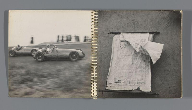 The image is a black and white photograph from an open spiral-bound album. On the left side of the spread, there's a blurry action shot depicting two vintage racing cars on what appears to be a race track; one car in motion with its wheels blurred due to speed, while another parked behind it. In front of these vehicles, slightly out-of-focus and likely moving at high speed is a person wearing a helmet and driving the nearest vehicle.

On the right side, there's an open page with various scraps of paper attached or pinned onto it by what seems like thumbtacks. The topmost piece has text that reads "MALA...", which could be part of a larger word but is cut off from view. Below this are additional bits and pieces of newspaper clippings or printed material, some partially overlapping others, creating an assortment of text snippets and possibly headlines. These items seem to have been collected as souvenirs or for reference.

The overall condition appears aged with creases on the pages indicating frequent use. The photograph has a documentary feel, likely capturing moments from events covered by Ed van der Elsken, as referenced in the source URL which mentions Aankondiging van een kermis (Announcement of a Fair), dated between c. 1948 and c. 1951.
