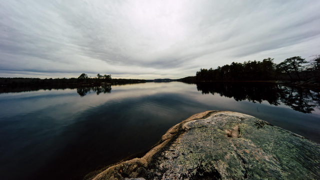In the lower right there is a big granite rock and past that a smooth lake reflecting stratus clouds and trees that line it
