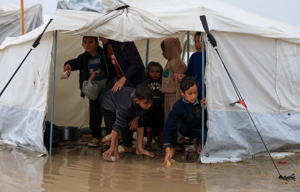 Displaced Palestinian children attempt to clear rainwater from a flooded tent.