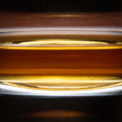 A photograph of a thin band of whisky in the bottom of a rocks glass, cropped to show only a bit of the whiskey in a band with glass and reflections above and below, giving the effect of the bands of gas in Jupiter's atmosphere.