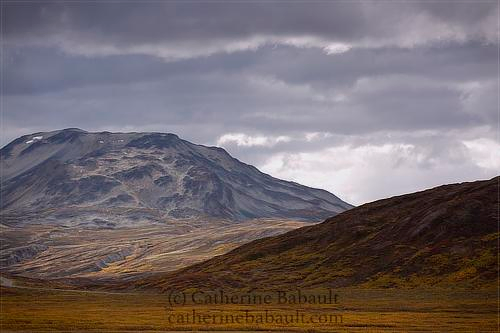 View of bare mountains with short vegetation in fall colours at lower altitude. The sky is grey and very cloudy.