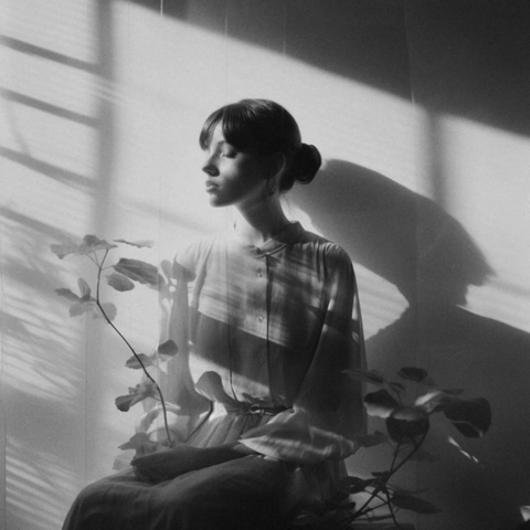 les yeux clos dans les premiers rayons du soleil venant de la fenêtre, une femme assise tenant un branchage